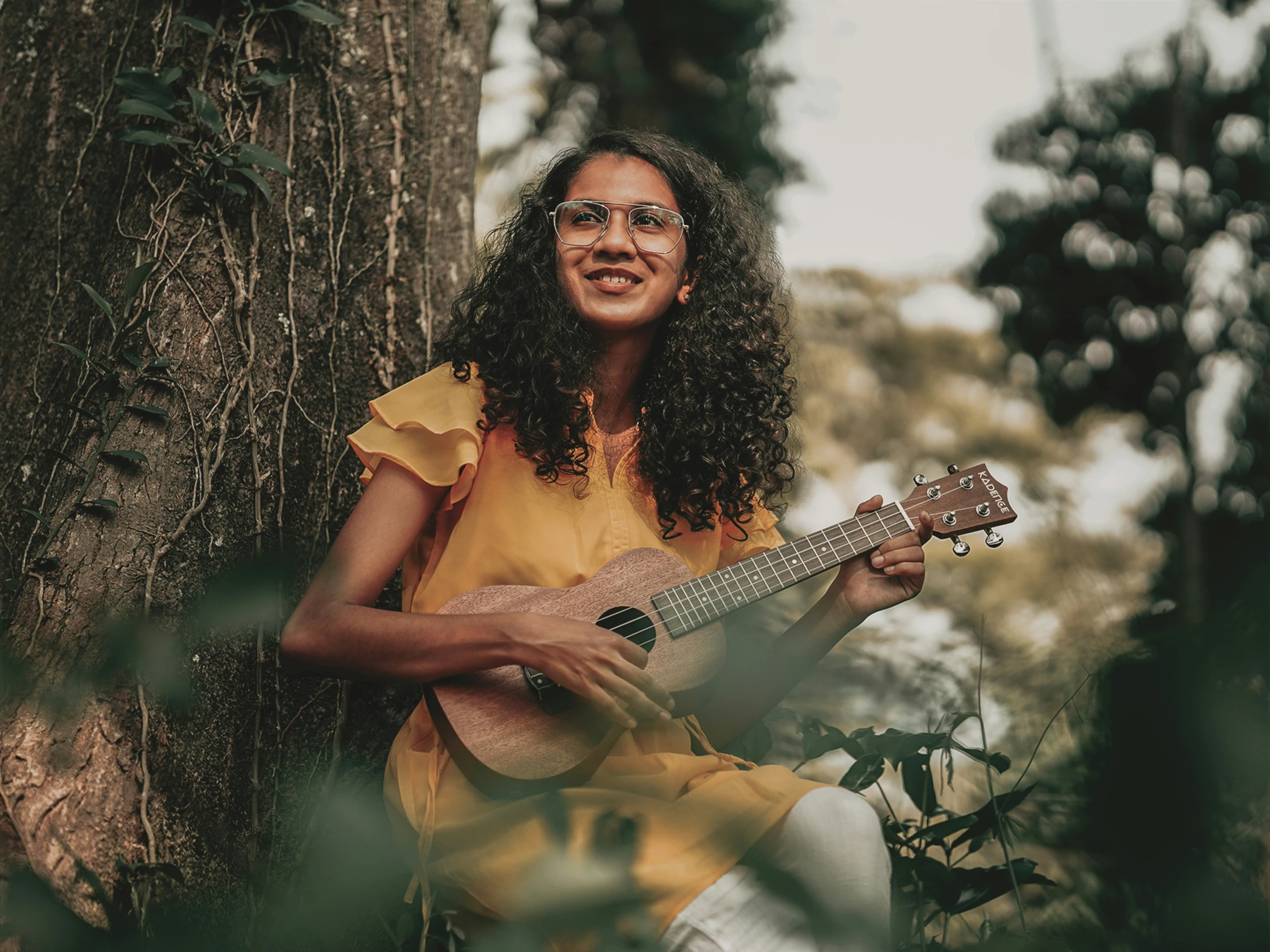 a smiling woman playing a guitar near trees