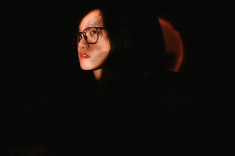 a woman with glasses on staring ahead while in the dark