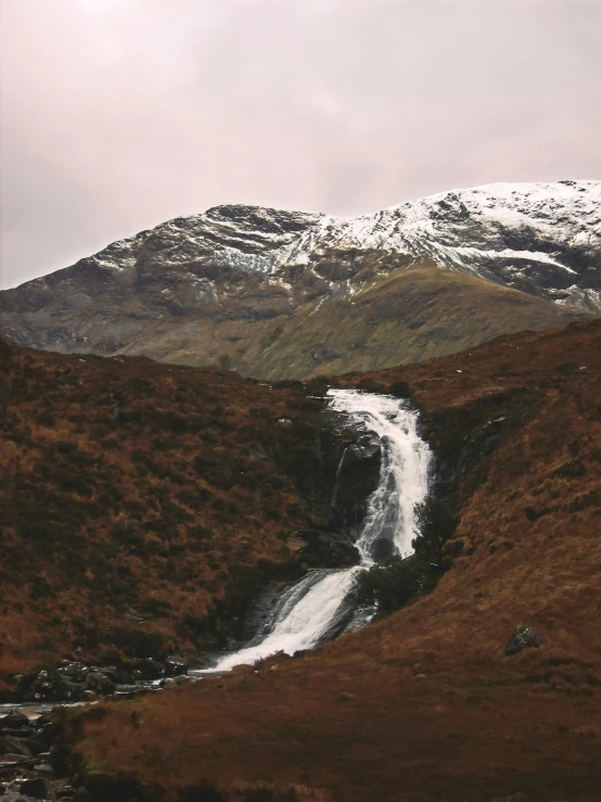 a stream cuts through the mountains with a small snow covered hill behind it