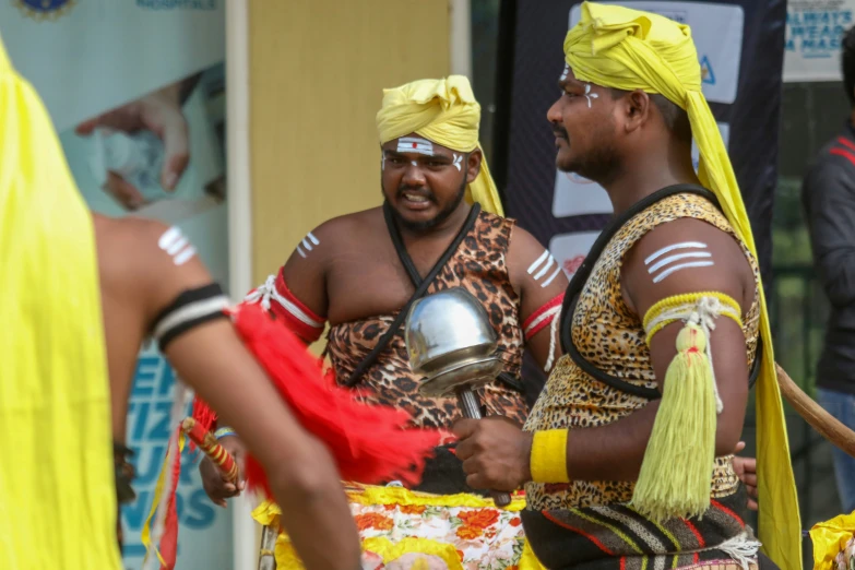 two men dressed in native attire holding metal items