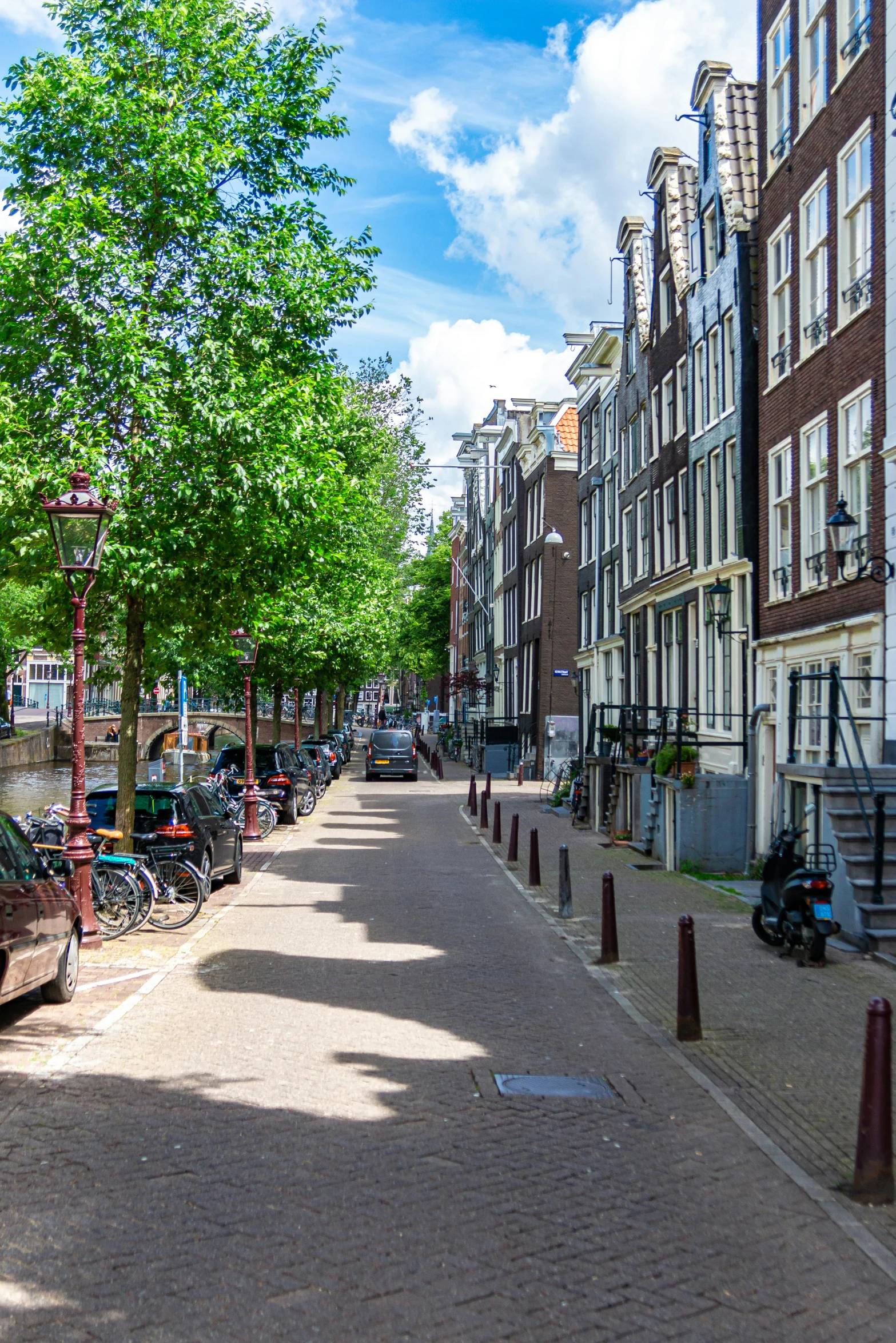 a very long brick street with some parked cars and a light pole on each side