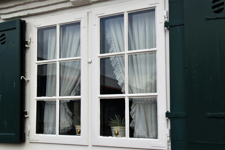 the open window is displaying white curtains and a potted plant