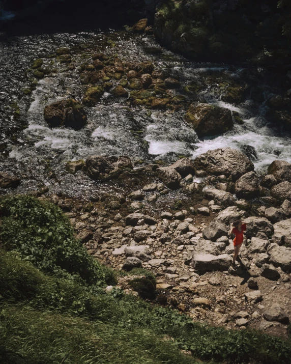 a person in a red shirt standing on rocks near water