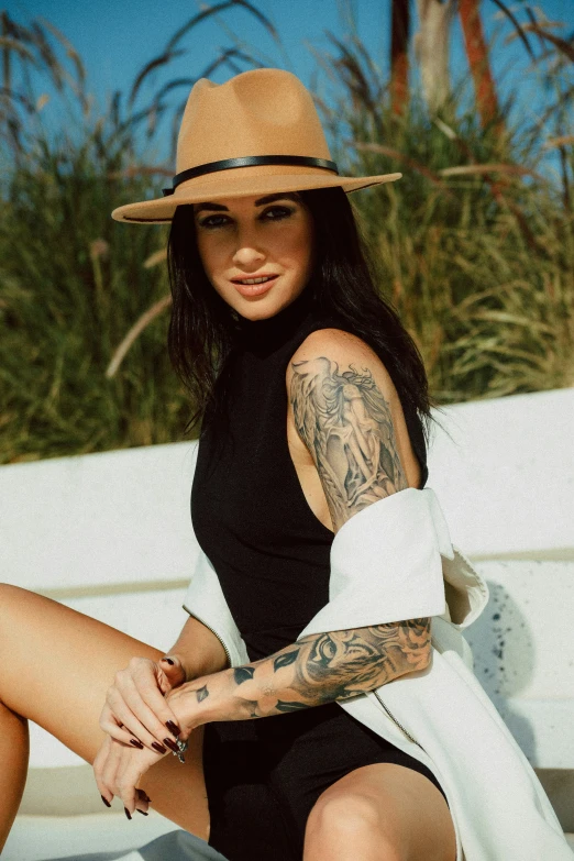 a woman with tattoos on her arm, wearing a hat and black dress