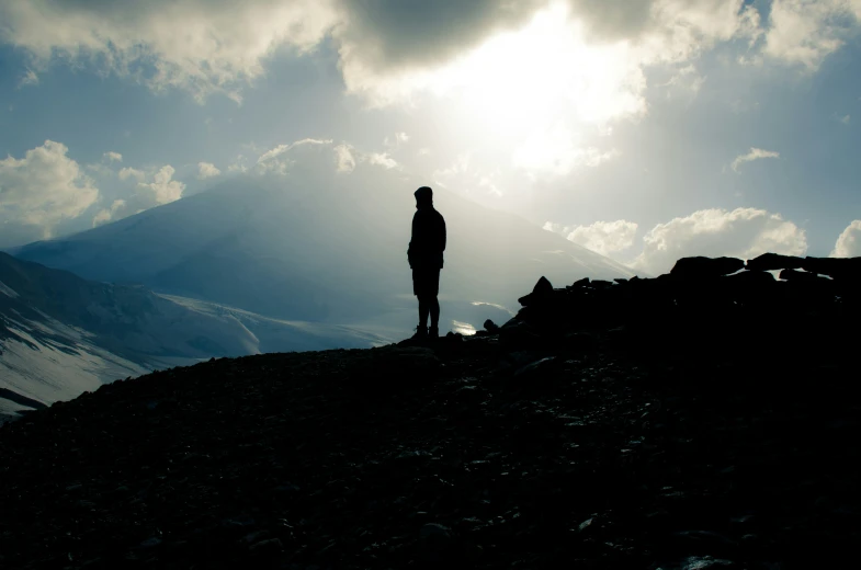 a man standing on top of a large hill under a sunlit sky