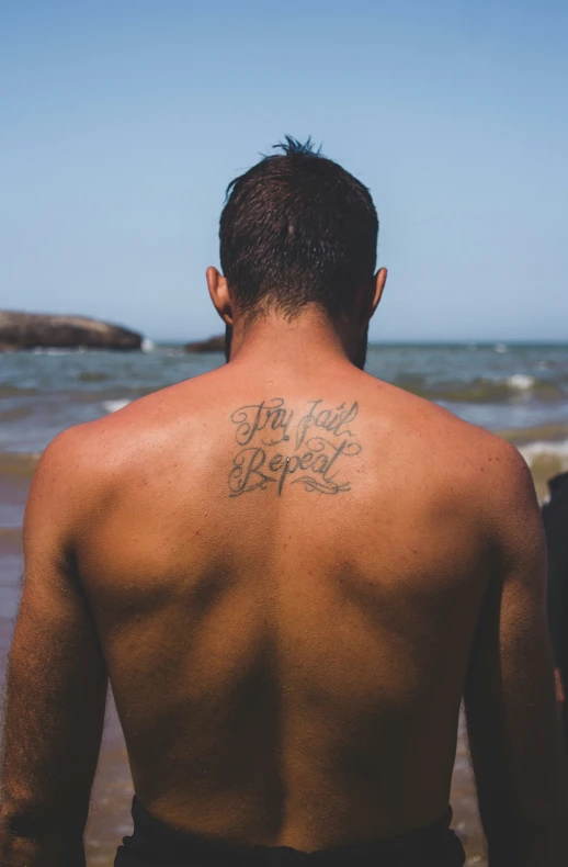 a shirtless man standing on the beach with his back turned