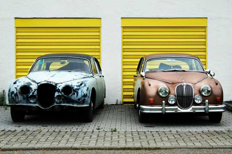 two old fashion looking cars in front of a yellow garage door