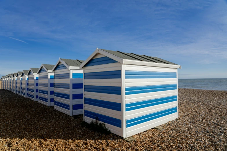 a row of blue and white beach huts sitting on top of a pebble covered ground