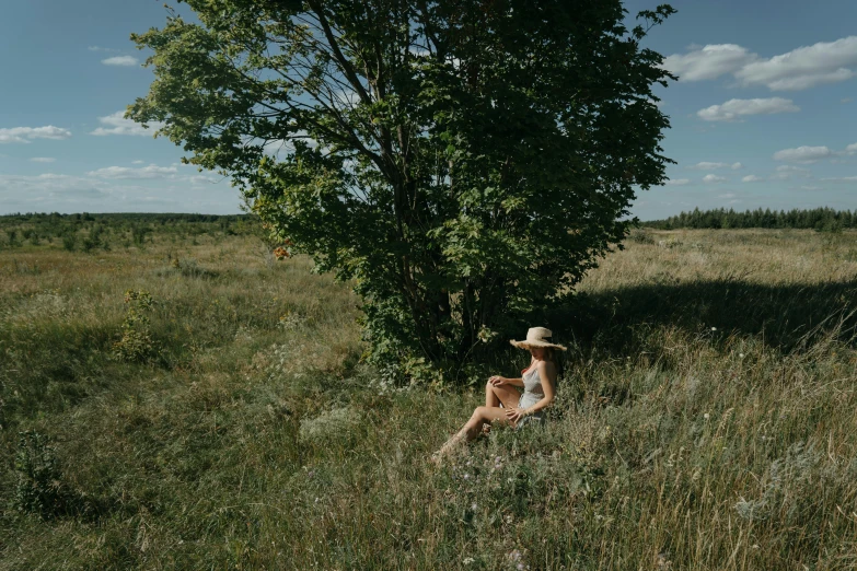 a woman sitting in a grassy field by a tree