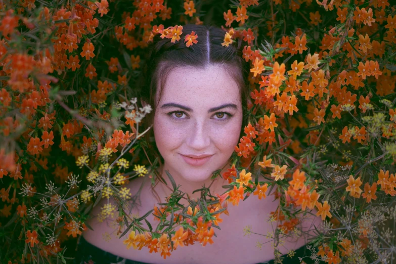 a woman with long hair and green eyes stands in front of flowers