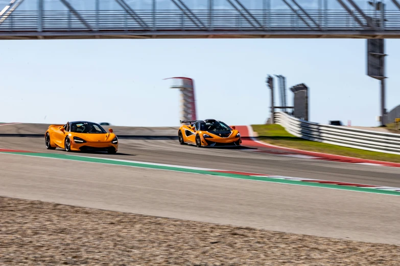 two yellow sports cars driving down a track under a bridge