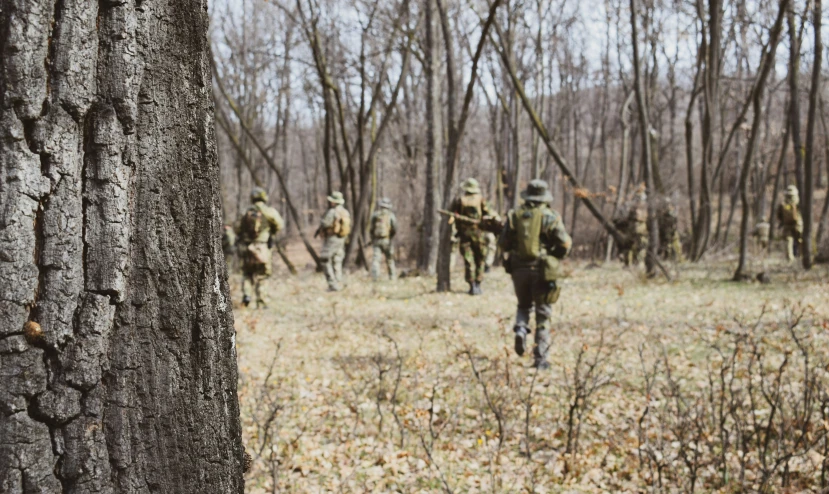 men in uniforms run through a field in front of trees