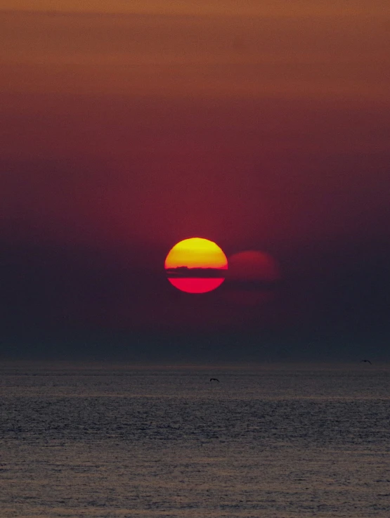 a red sun is rising over a calm sea