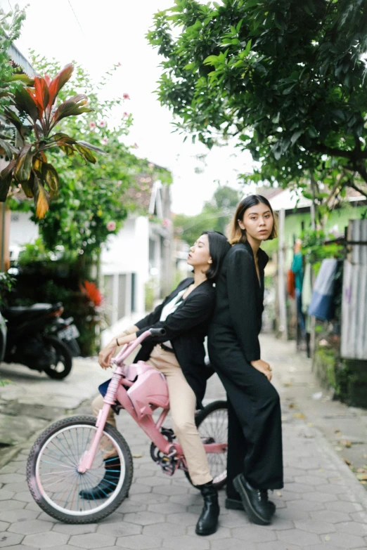 two women and a man riding on a pink bicycle