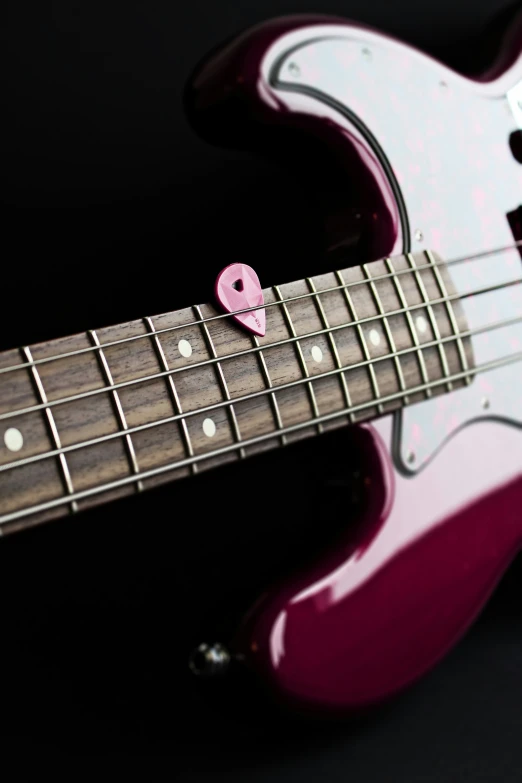 a small heart shaped pink object sits on top of the neck of a guitar