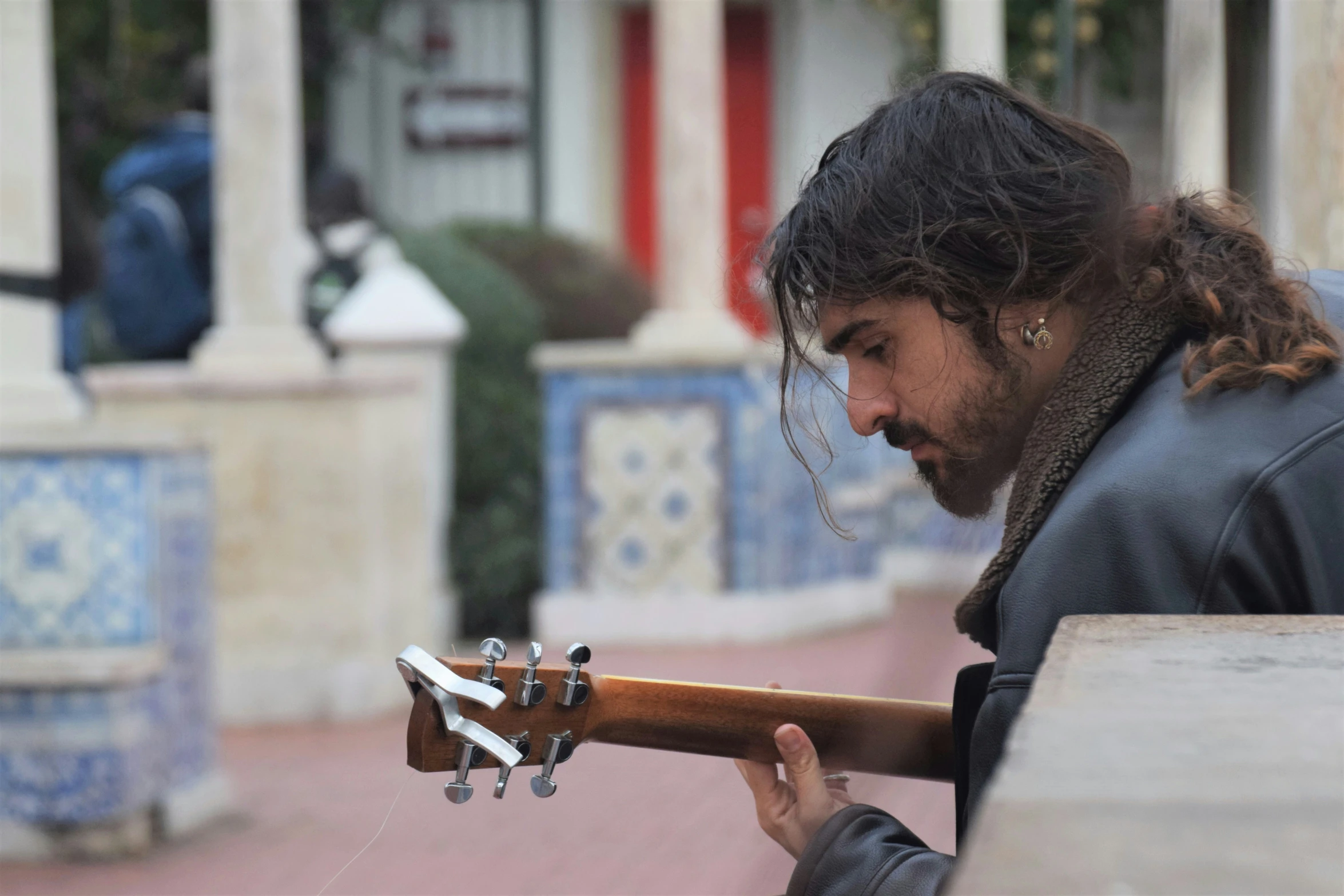 a man playing guitar outside a building with an umbrella