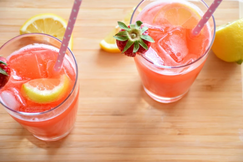 two glasses of strawberry soda sit next to some sliced lemons