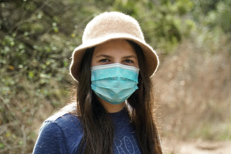 a woman wearing a mask and hat, in a park