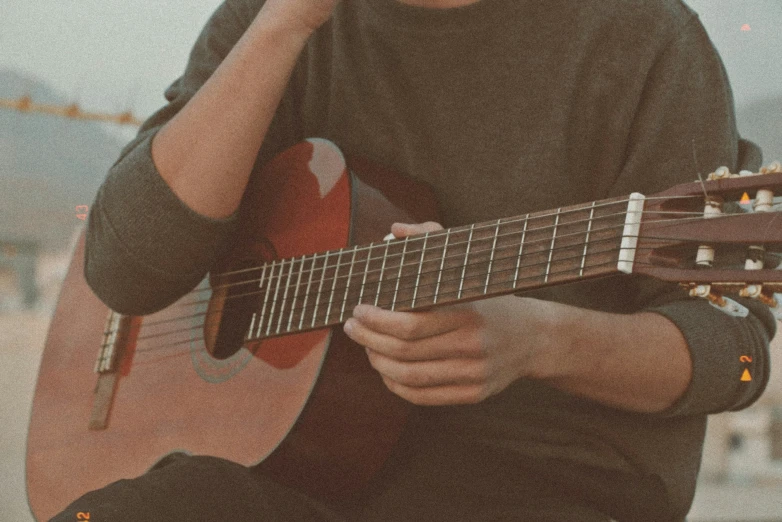 a man sitting and playing guitar in front of a mountain