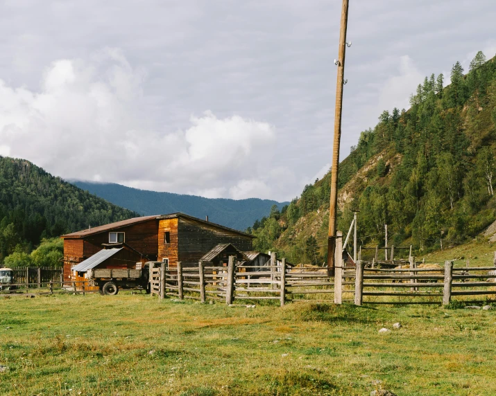 an old cabin on a hillside with an over sized fence