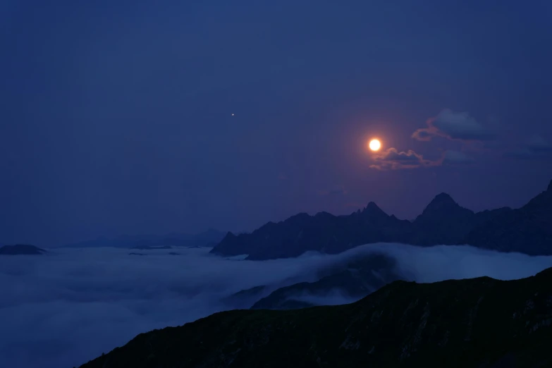 the moon setting over a fog filled mountain range