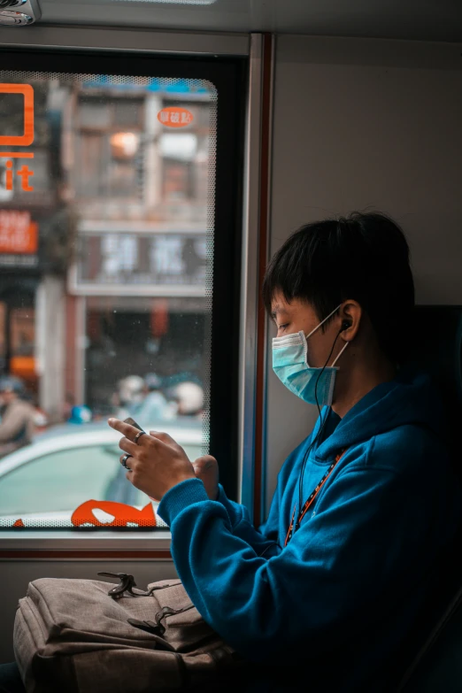 a woman in a face mask on a train while looking at her cell phone