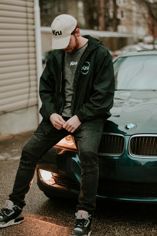 a person wearing sneakers sits on the hood of a parked car