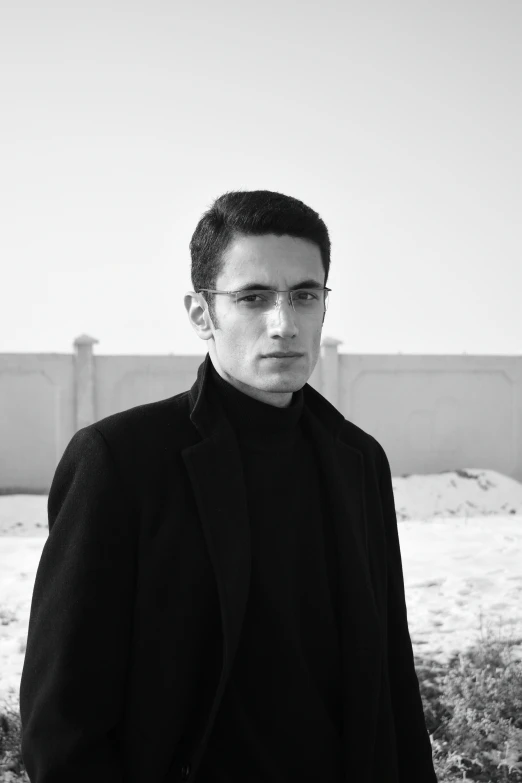 a man in a black suit poses on the beach