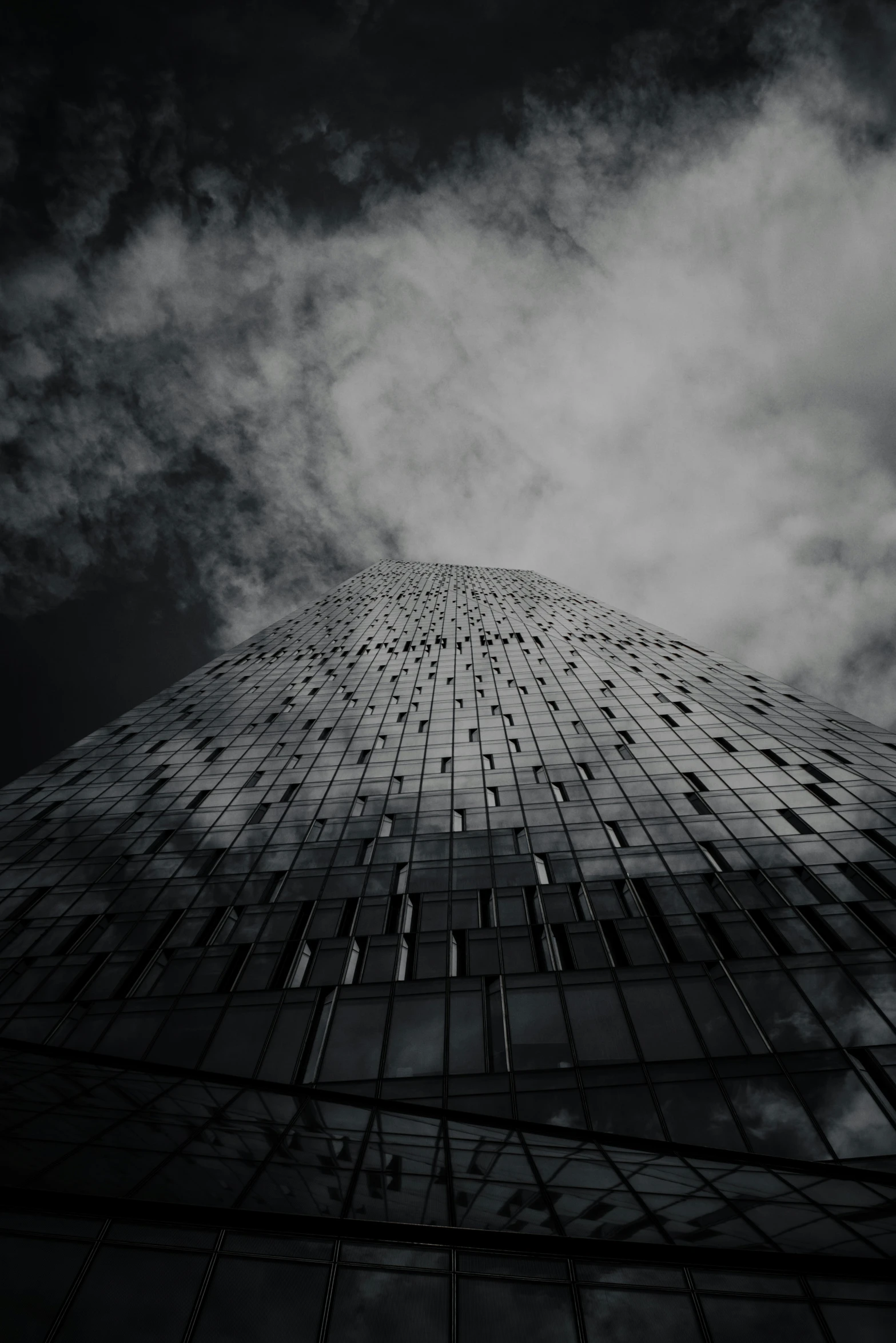 a tall glass building with cloudy skies above it