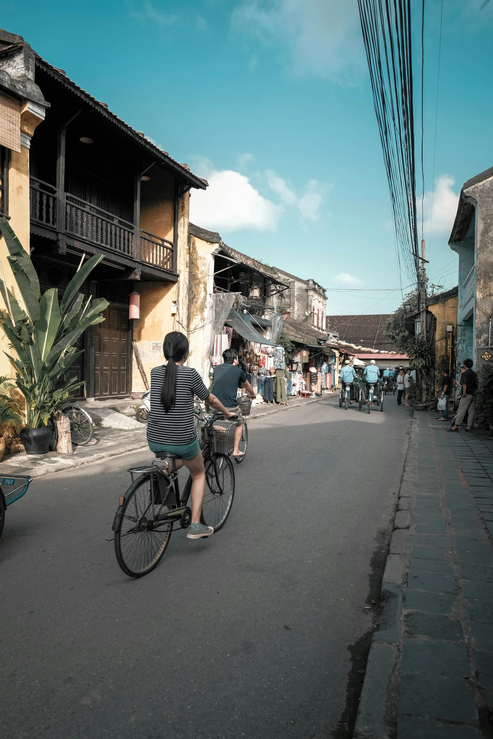 three people riding bicycles on a street past small houses