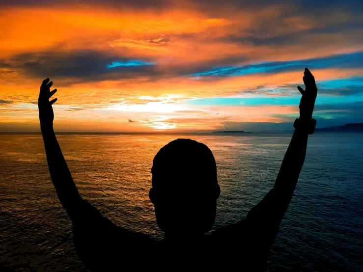 the silhouette of a person reaching up to the sky with his hands in the air