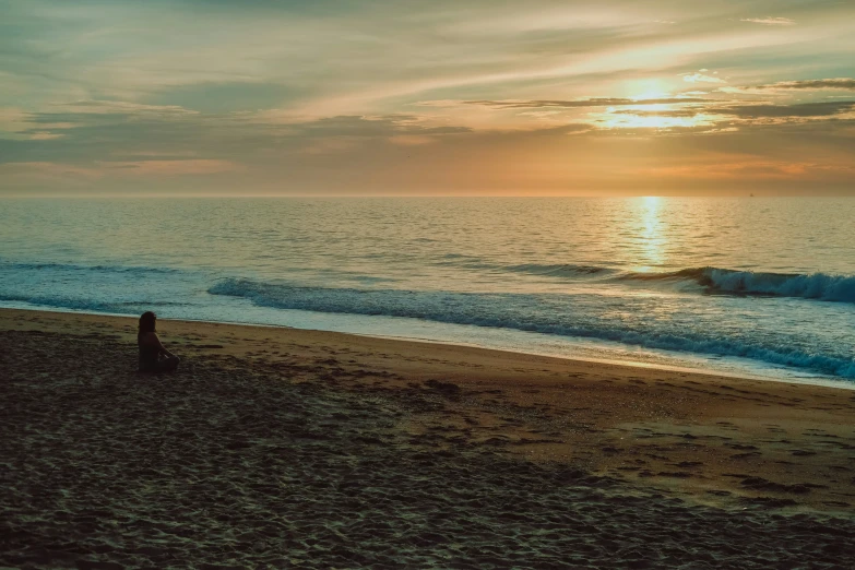 the ocean is on a sandy beach at sunset