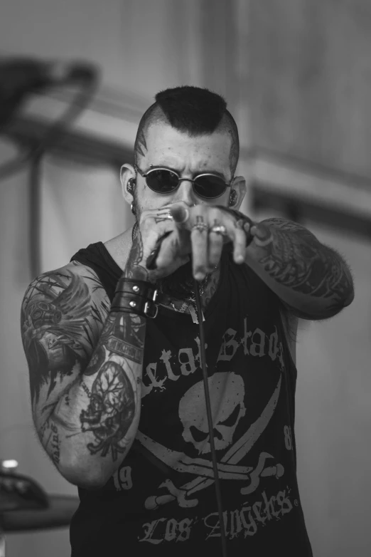 a man with tattoos standing up holding a microphone and pointing