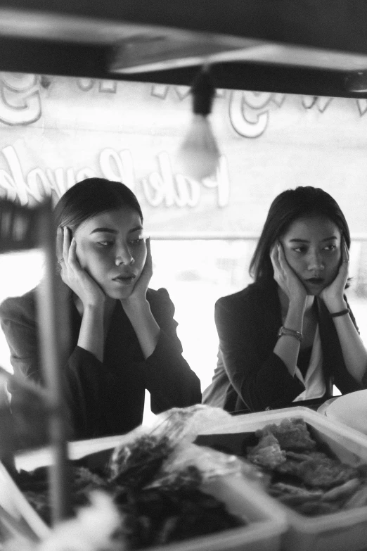 two people sit at a table while a girl in glasses talks on her cell phone