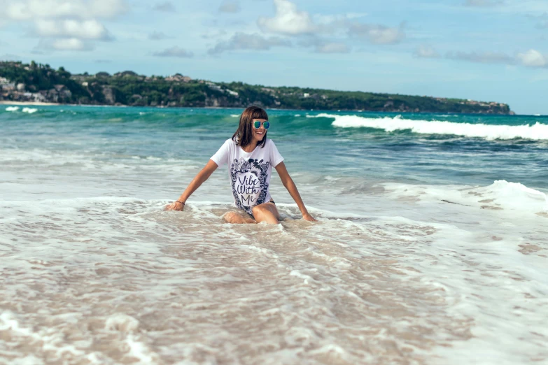 a girl sitting on the sand at the ocean's edge