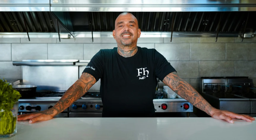 a man in a black shirt behind a counter with a green pepper