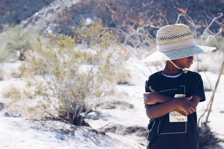 a little boy with a hat on standing next to a bush