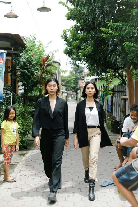 two women walking down a sidewalk while people look on