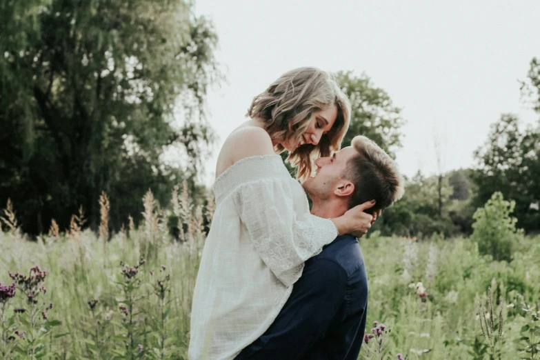 a man holding his face up to his girlfriend in the middle of a field