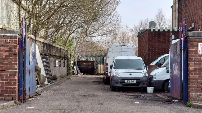 two trucks parked at the entrance to an alley with other cars parked in the alley