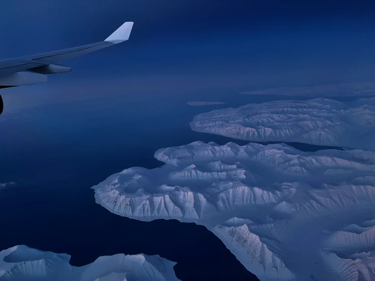 the wing of an airplane above the ocean and snow