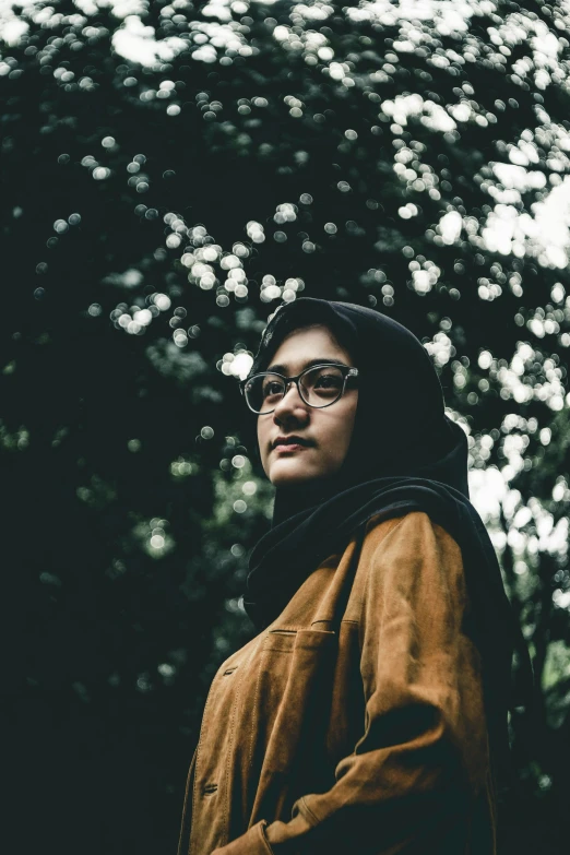 a man in a brown hooded sweatshirt and black glasses looking off into the distance