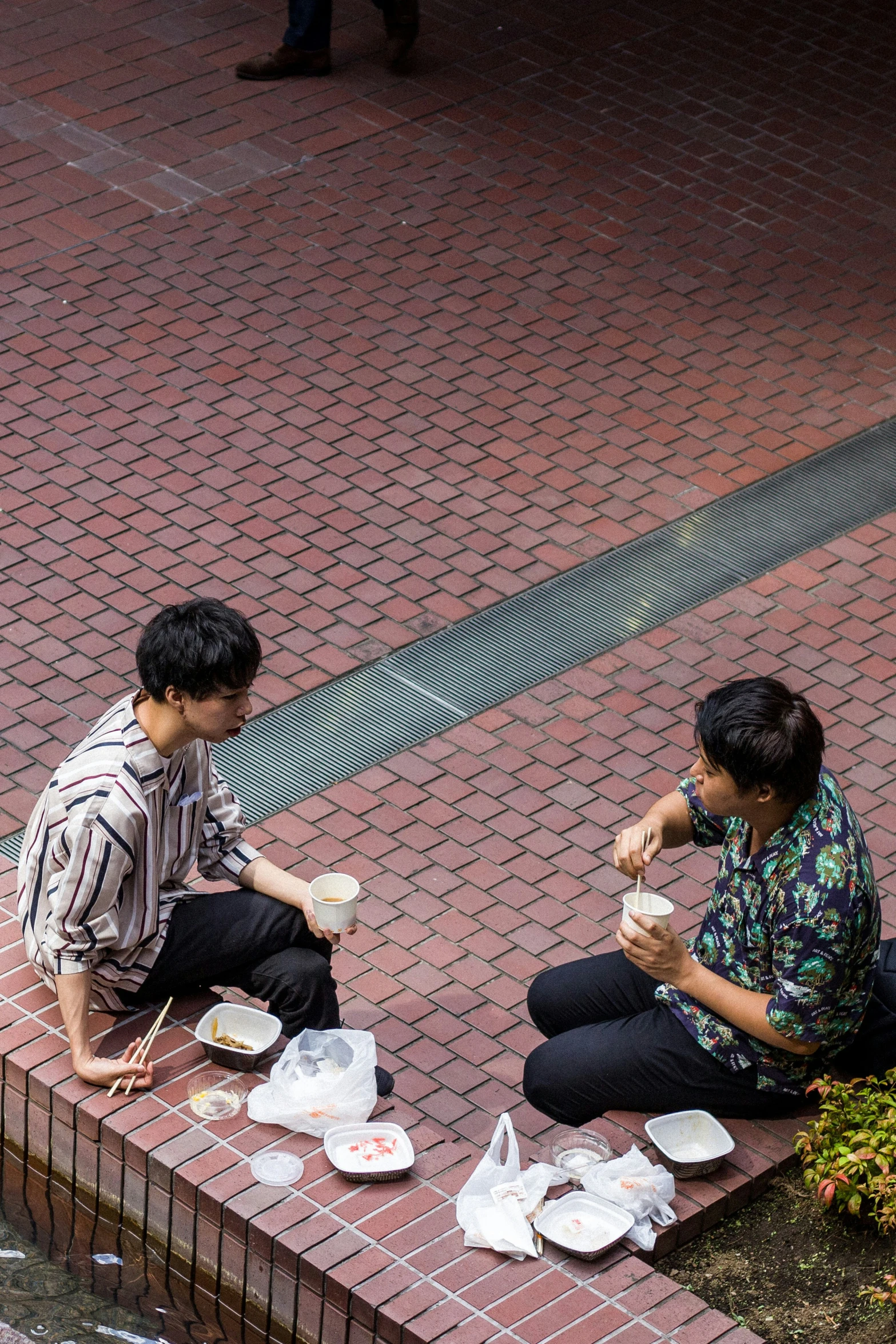 two asian men eating in front of a red brick sidewalk