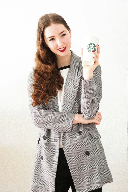 woman standing in front of a white background posing with her hand on the cup