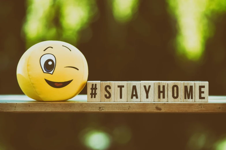 a small emoticment sits on top of some scrawled words that spell out stay home