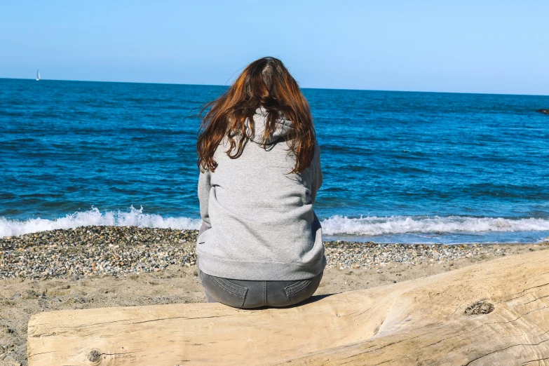 the girl is sitting on a rock alone by the ocean