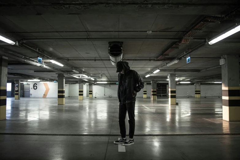 man in black jacket skateboarding under a large parking lot