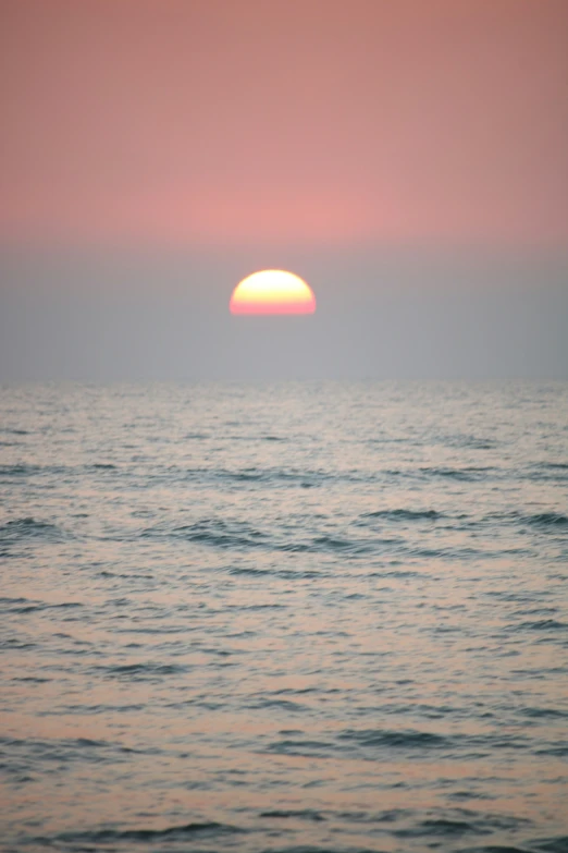 the sun rising over the ocean with calm water