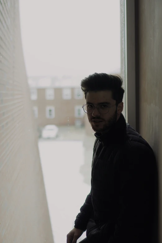 a man wearing glasses, leaning against a wall