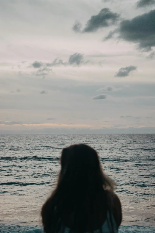 a woman standing in the ocean looking at the clouds